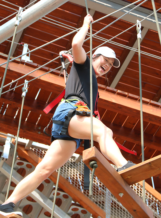 Young female crossing a challenge on ropes course with big smile at a birthday party